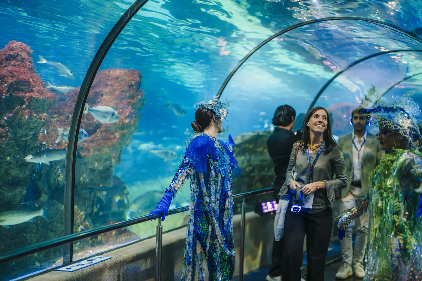 Guía con vestuario marino acompaña a un grupo por el túnel acuático durante un recorrido exclusivo de L’Aquàrium.