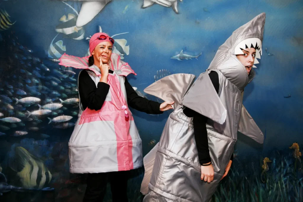 Two actors dressed as marine creatures pose in front of an underwater backdrop during a theatrical educational activity.