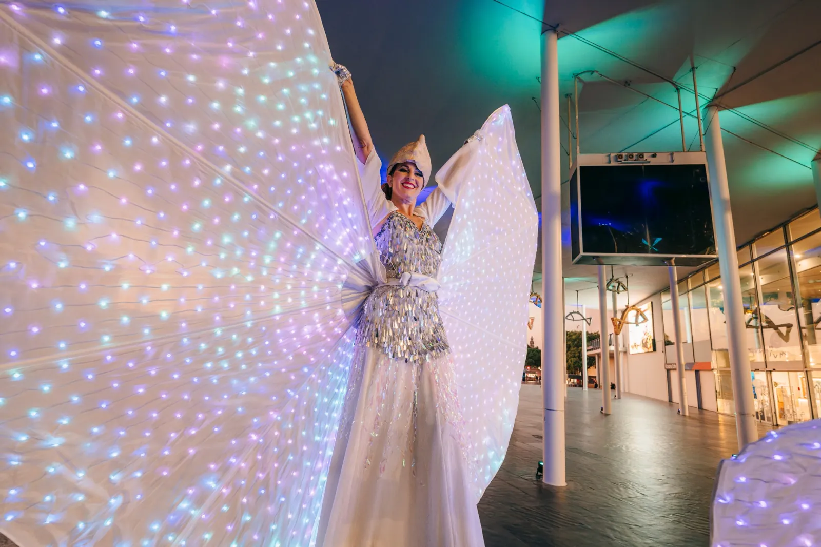 Artistas con alas luminosas reciben a los invitados en una zona interior de L’Aquàrium durante un evento.